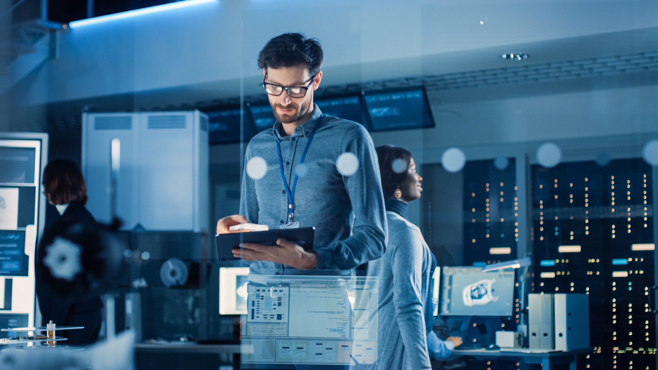 In Technology Research Facility: Chief Engineer Stands in the Middle of the Lab and Uses Tablet Computer. Team of Industrial Engineers, Developers Work on Engine Design Use Digital Whiteboard and Computers