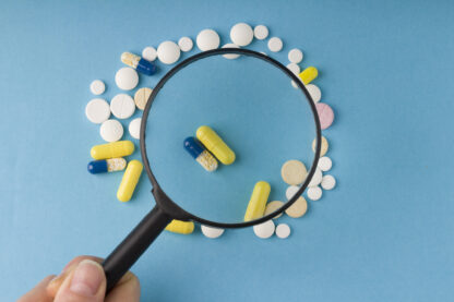 female hand holds a magnifying glass over pills